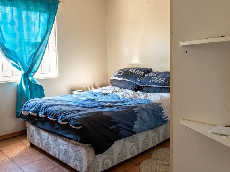 A compact bedroom featuring tiled flooring, built-in shelving, and a window fitted with security bars.
