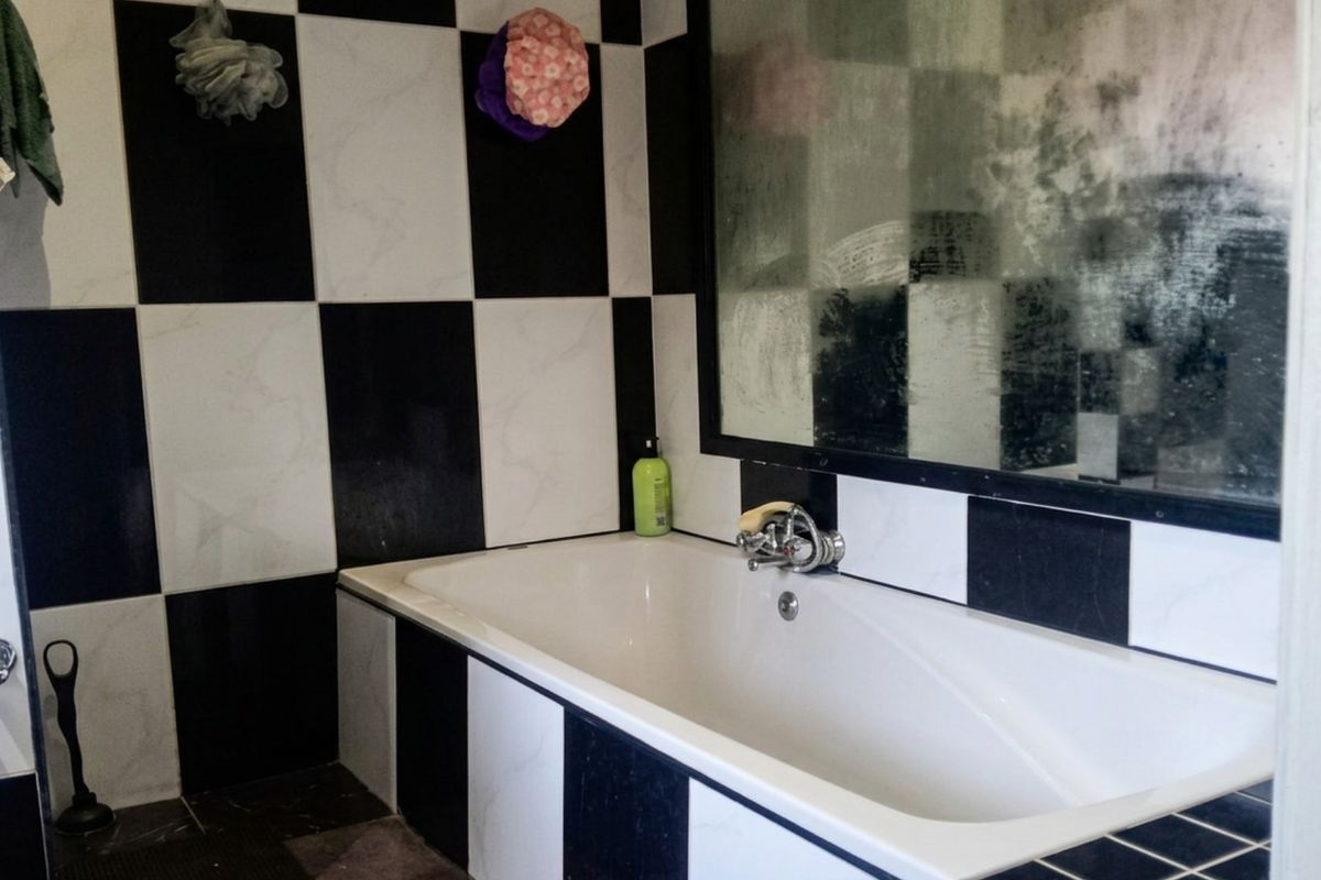 A bathroom featuring a bathtub with black and white checkered wall tiles and a large wall-mounted mirror.