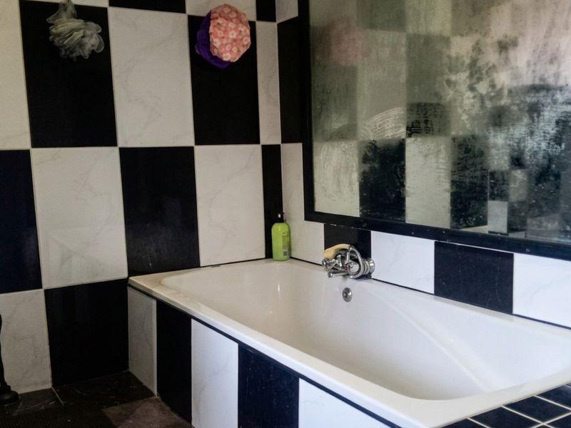 A bathroom featuring a bathtub with black and white checkered wall tiles and a large wall-mounted mirror.