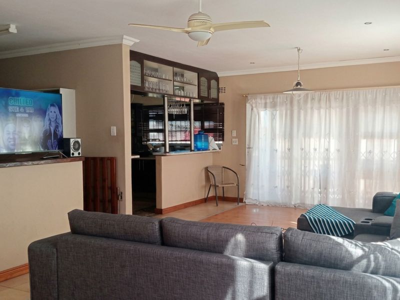 Spacious open-plan living area featuring a built-in bar with glass cabinetry, ceiling fan, tiled floors, and direct access to the outdoors via sliding doors.