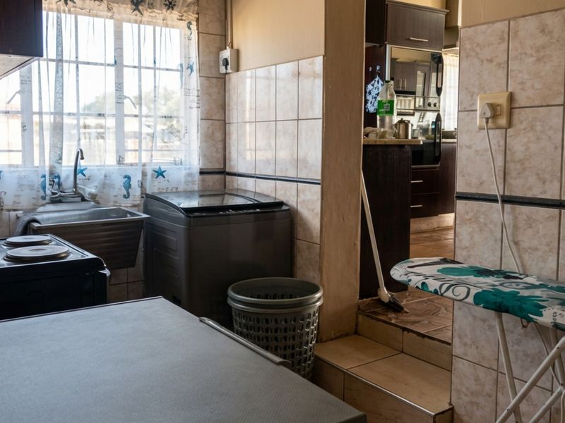 A functional laundry area featuring tiled walls, a stainless steel sink, and direct access to an adjacent kitchen space.