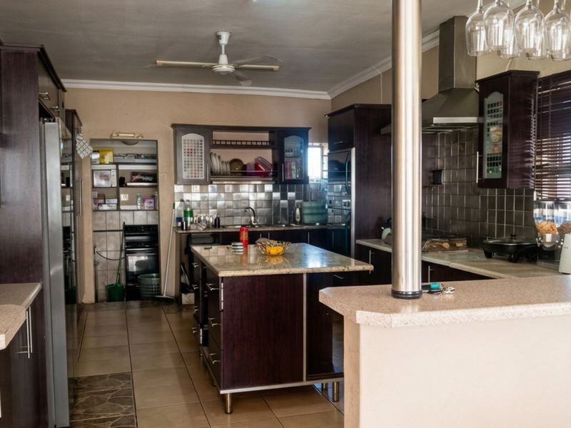 Spacious kitchen featuring dark wood cabinetry, granite countertops, a central island, breakfast bar, and a tiled backsplash with integrated extractor fan.