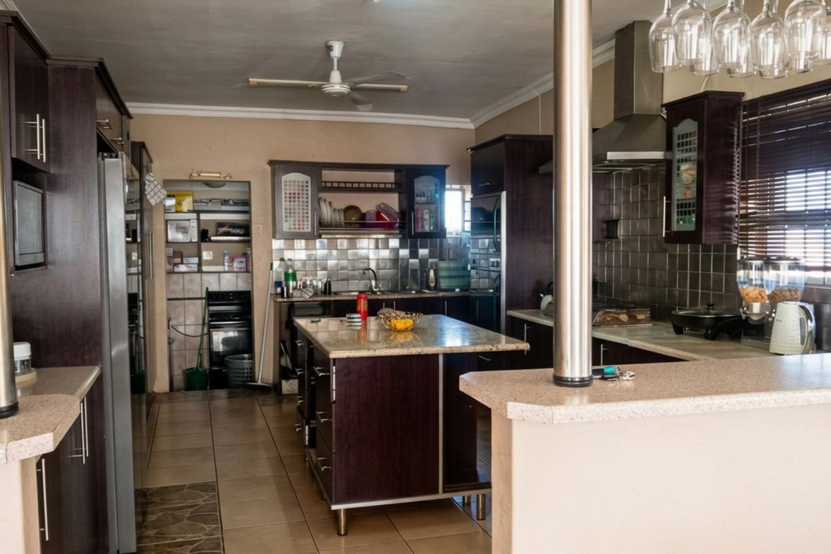 Spacious kitchen featuring dark wood cabinetry, granite countertops, a central island, breakfast bar, and a tiled backsplash with integrated extractor fan.