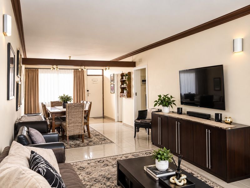 Spacious open-plan living and dining area featuring neutral walls, tiled flooring, crown molding, and an exposed ceiling beam, creating a cohesive and inviting atmosphere.