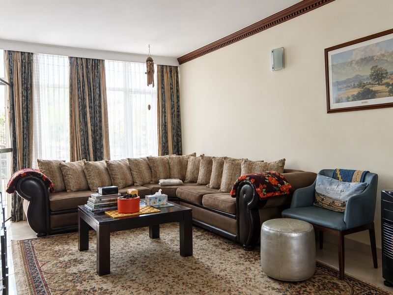 A comfortable living room featuring crown molding, wall sconce lighting, and large floor-to-ceiling windows that provide ample natural light.