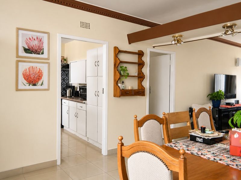 Open plan living and dining area featuring tiled floors, crown molding, and an exposed ceiling beam, with an adjacent kitchen visible through the doorway.