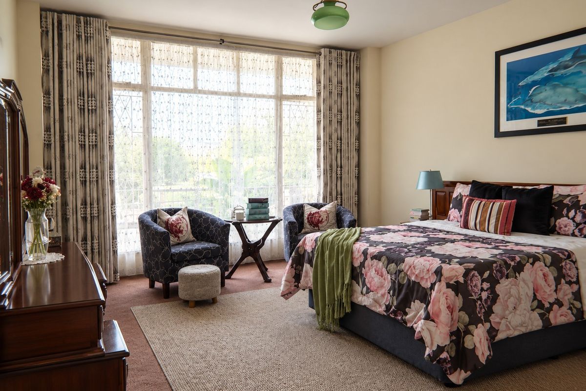 A spacious bedroom featuring a large window with natural light, neutral wall finishes, and carpeted flooring.