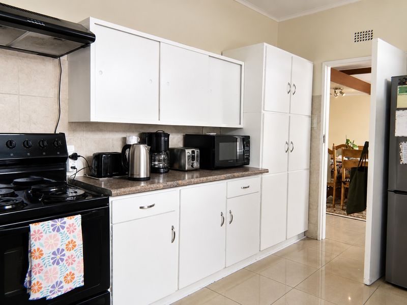 A functional kitchen featuring white built-in cabinetry, laminate countertops, tiled backsplash, and ceramic floor tiles, with an adjacent view into the dining area.
