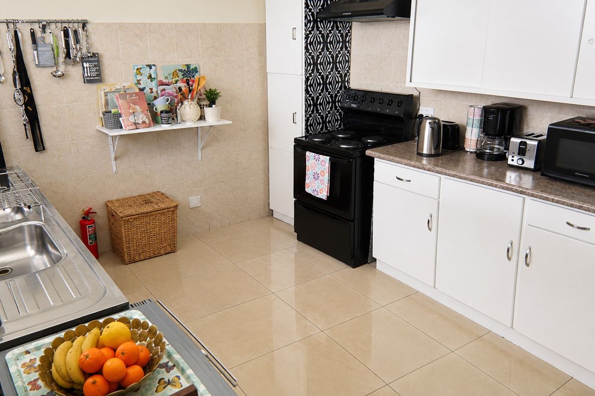 A functional kitchen featuring white cabinetry, tiled backsplash, laminate countertops, and a built-in electric stove with an extractor fan.