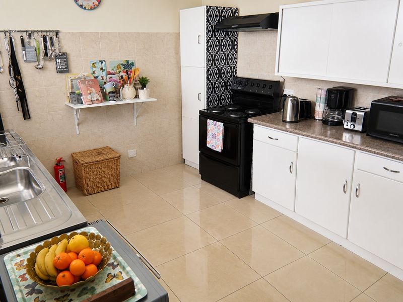 A functional kitchen featuring white cabinetry, tiled backsplash, laminate countertops, and a built-in electric stove with an extractor fan.