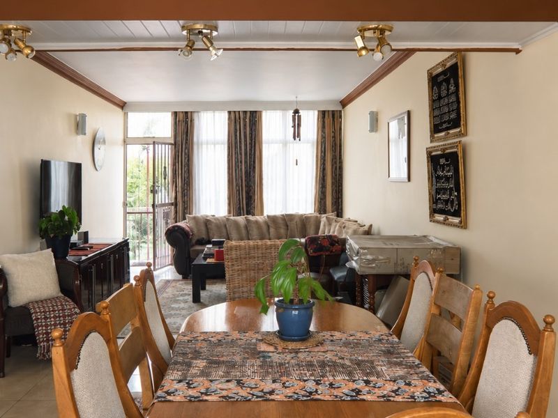 Open-plan living and dining area featuring tiled floors, exposed ceiling beams, and natural light through a sliding glass door.