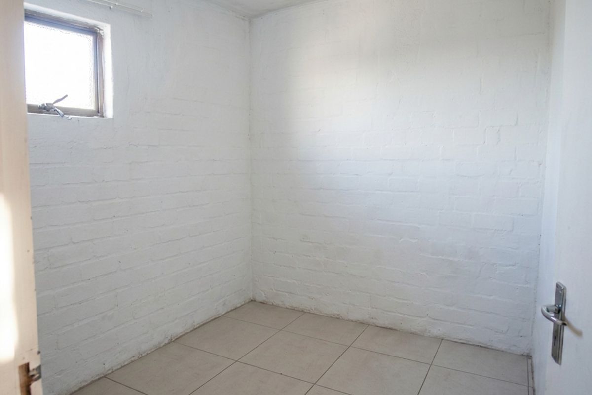 A compact, empty bedroom featuring white-painted brick walls, tiled flooring, and a small casement window, offering a blank canvas for renovation.