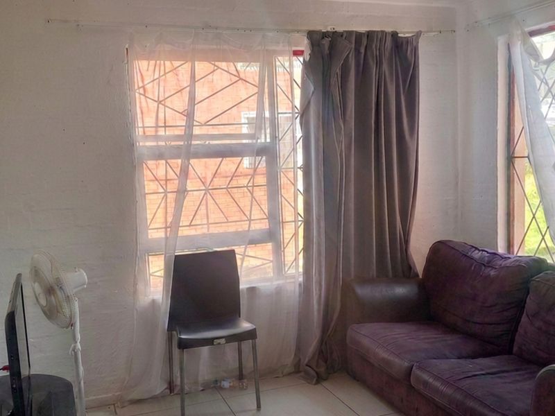 A living room area featuring tiled flooring and windows fitted with security bars, requiring cosmetic updates to improve the overall finish.