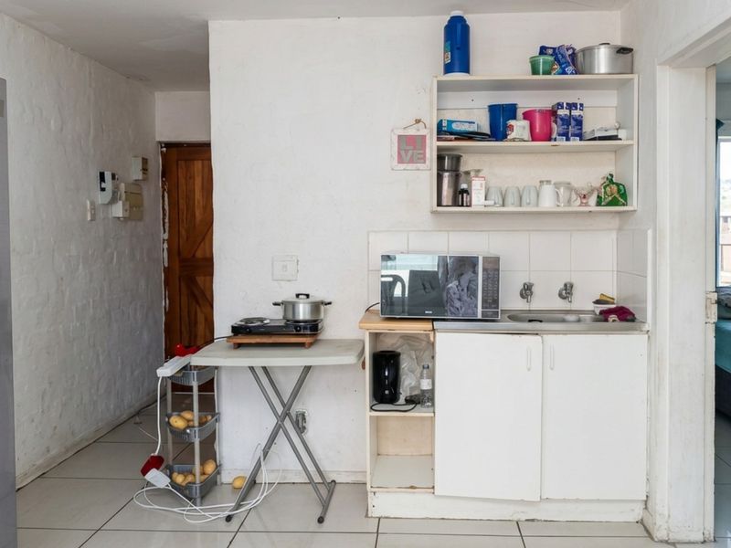 A compact kitchen area featuring basic cabinetry, a sink, and tiled flooring, currently requiring significant cosmetic updates and modernization.
