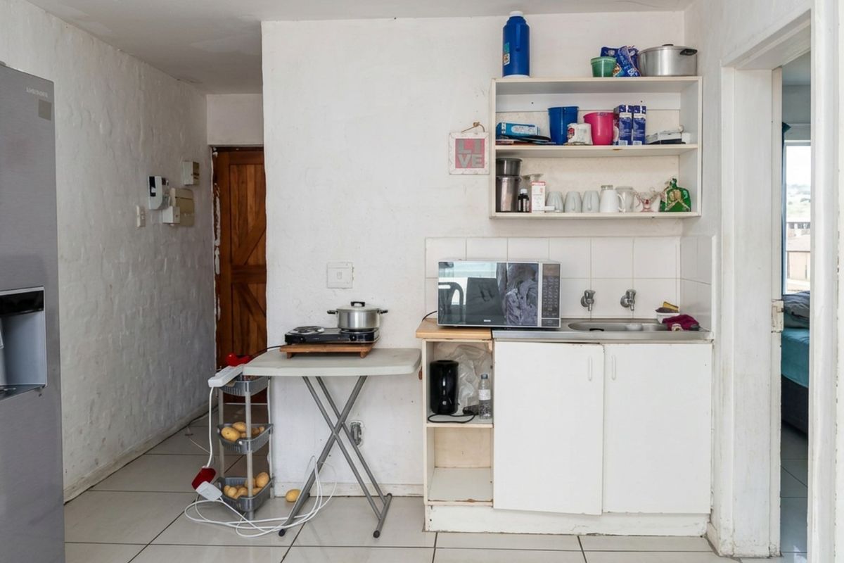 A compact kitchen area featuring basic cabinetry, a sink, and tiled flooring, currently requiring significant cosmetic updates and modernization.