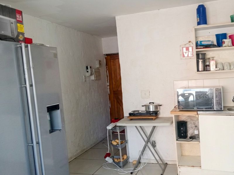 A compact kitchen area featuring basic cabinetry, open shelving, a sink, and tiled flooring, offering potential for modernization and improved storage solutions.