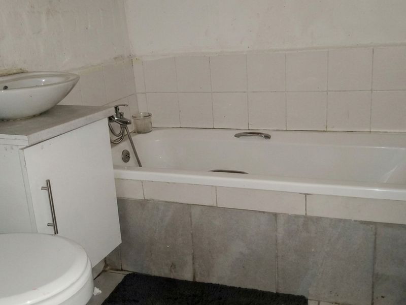 A compact bathroom featuring a built-in bathtub, vanity basin, and toilet, requiring cosmetic updates to the wall finishes and tiling.