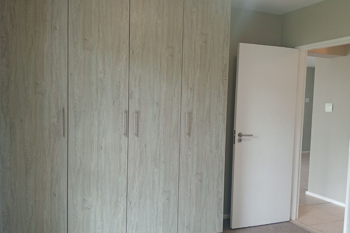 A clean bedroom interior featuring modern wood-look built-in cupboards and a neutral color palette, offering a bright and functional living space.