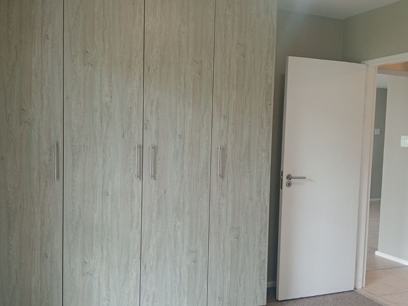 A clean bedroom interior featuring modern wood-look built-in cupboards and a neutral color palette, offering a bright and functional living space.