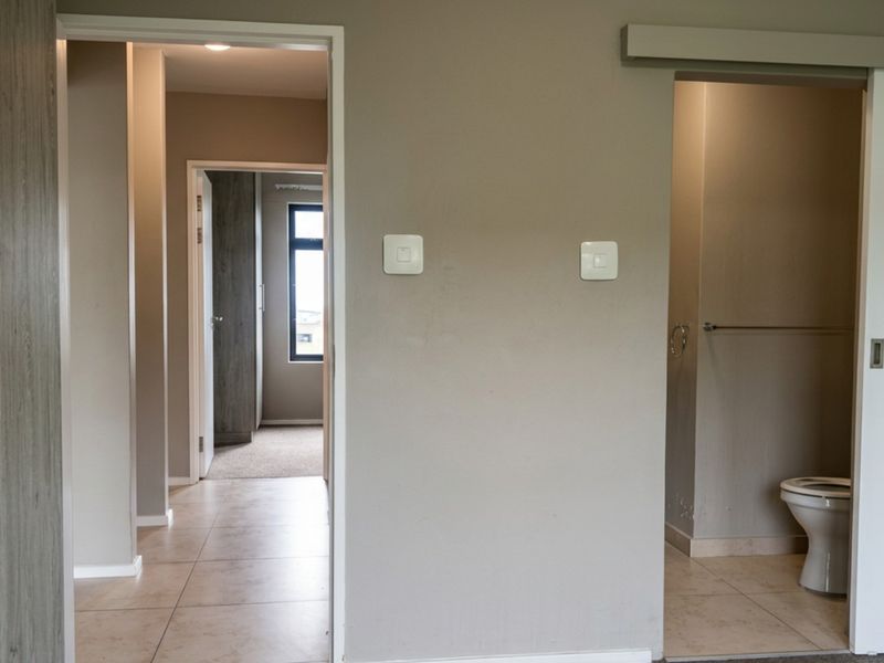 A clean, neutral-toned hallway featuring tiled flooring, built-in cabinetry, and a sliding door providing access to an adjacent bathroom.
