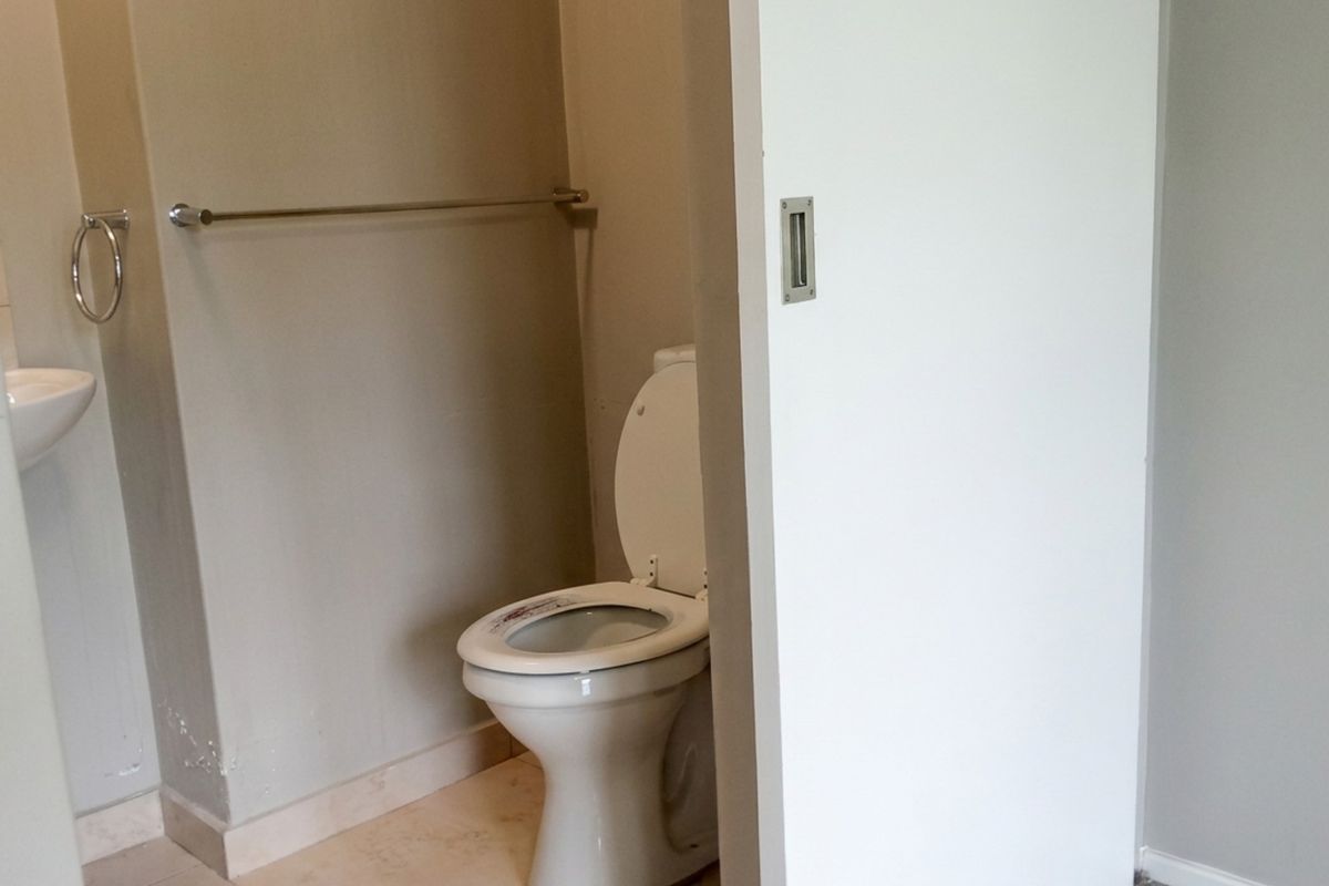 A compact bathroom featuring a toilet, wall-mounted basin, and a sliding door, showing signs of minor wear on the lower wall finishes.