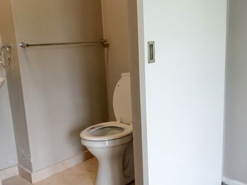 A compact bathroom featuring a toilet, wall-mounted basin, and a sliding door, showing signs of minor wear on the lower wall finishes.