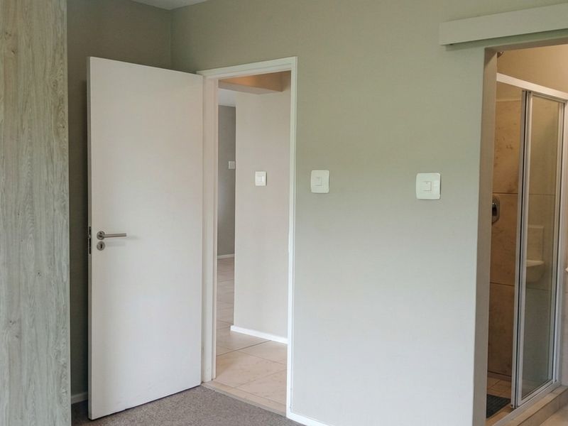 A clean bedroom featuring a built-in wardrobe and direct access to an en-suite bathroom with a shower and wall-mounted basin.