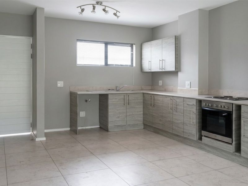 A clean, modern kitchen featuring light wood-grain cabinetry, integrated oven and hob, tiled flooring, and neutral grey walls.