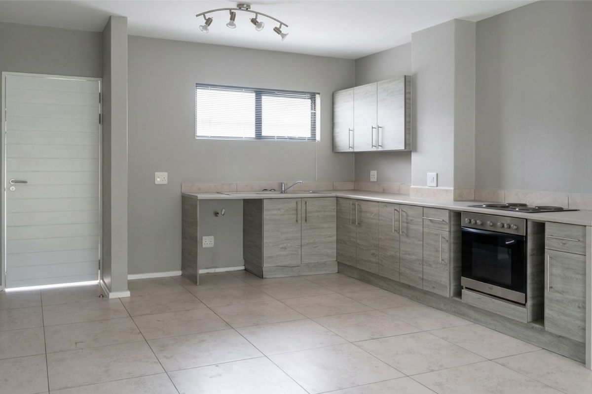 A clean, modern kitchen featuring light wood-grain cabinetry, integrated oven and hob, tiled flooring, and neutral grey walls.