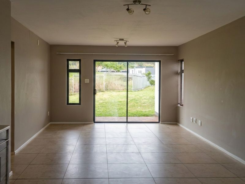 An open-plan living area featuring tiled floors, a sliding glass door leading to the garden, and a compact kitchen section with built-in appliances.