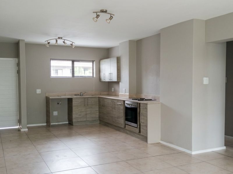 An open-plan living and kitchen area featuring neutral wall tones, tiled flooring, modern cabinetry, and a built-in oven with hob.
