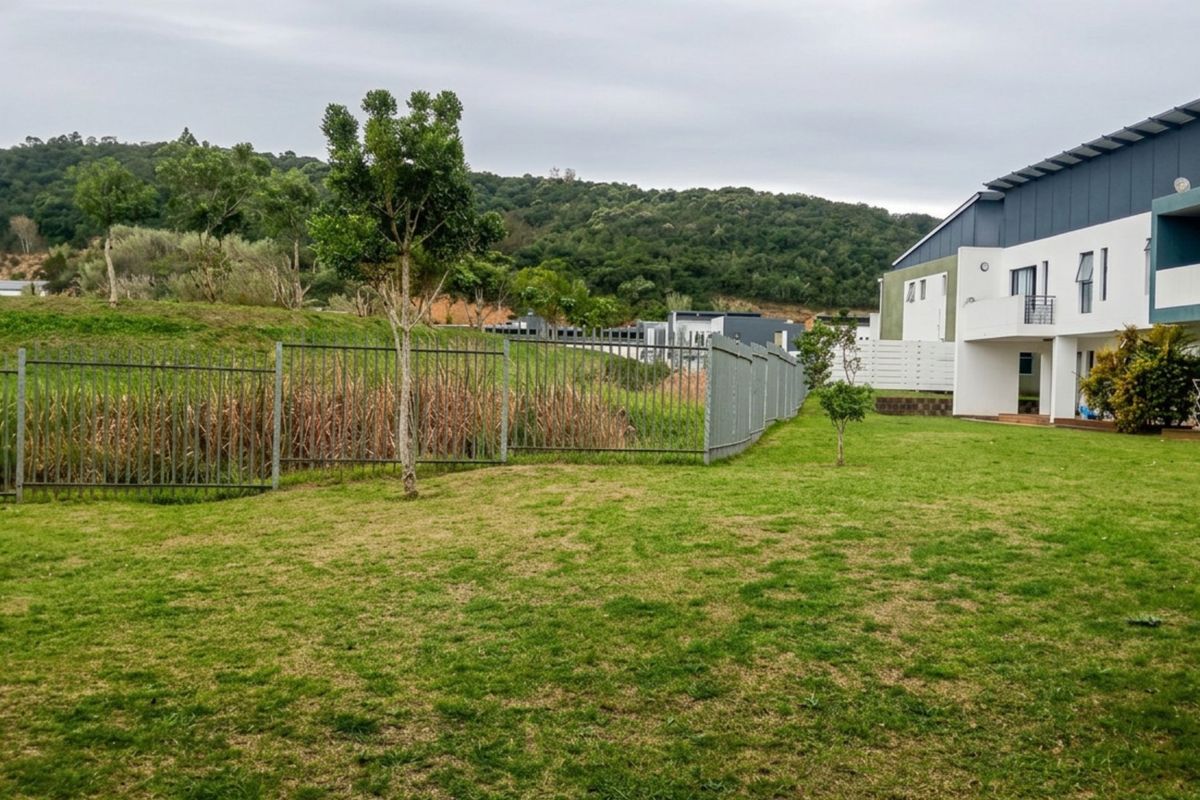 A view of the rear exterior of the apartment building, featuring a well-maintained lawn, metal perimeter fencing, and access to a private patio area.