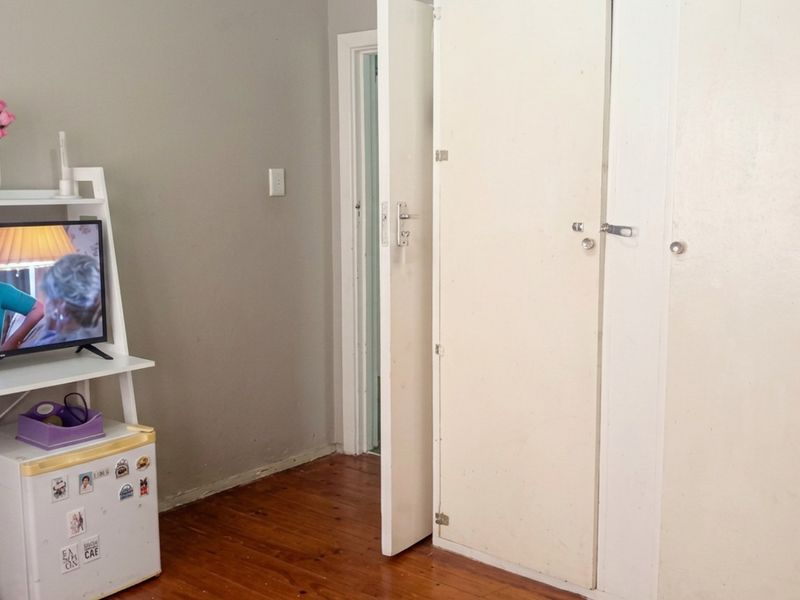 A bedroom featuring timber flooring and built-in cupboards, showing signs of wear and requiring cosmetic updates.