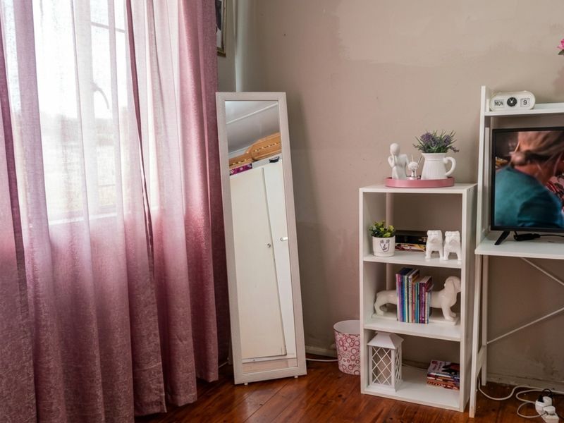 A bedroom featuring warm timber flooring and a large window with natural light, providing a comfortable and functional living space.