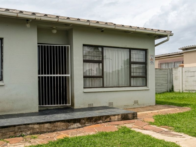 Rear exterior view of the house featuring a tiled patio, security gate, aluminium window frames, and a paved walkway leading to the garden.