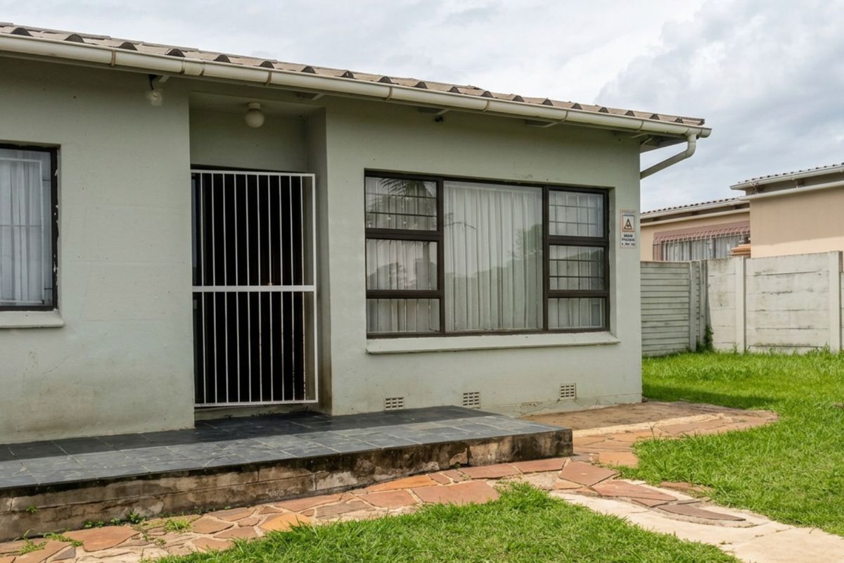 Rear exterior view of the house featuring a tiled patio, security gate, aluminium window frames, and a paved walkway leading to the garden.