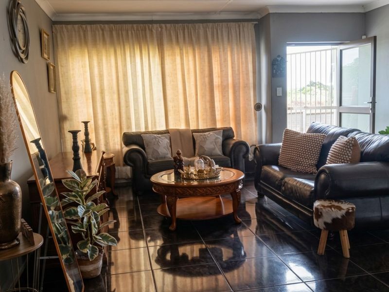 A comfortable living room featuring dark tiled flooring, neutral wall tones, and direct access to the exterior through a security-fitted sliding door.
