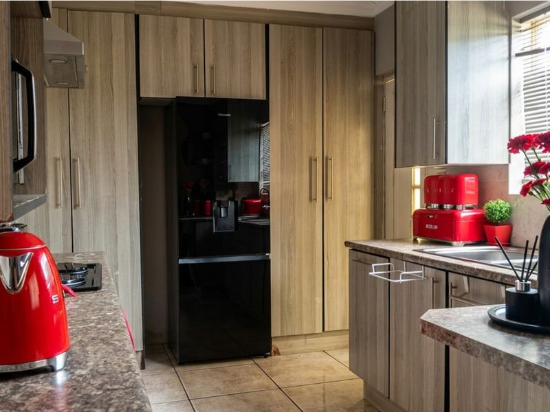 A functional kitchen featuring wood-look cabinetry, laminate countertops, integrated hob with extractor, and tiled flooring, providing a practical and well-maintained cooking space.