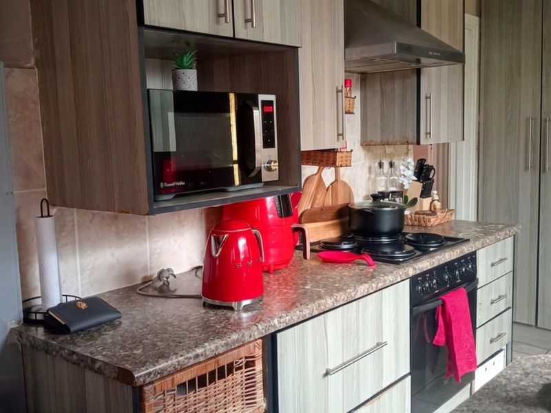 A functional kitchen featuring wood-look laminate cabinetry, a tiled backsplash, built-in oven, electric hob, and a stainless steel extractor fan.