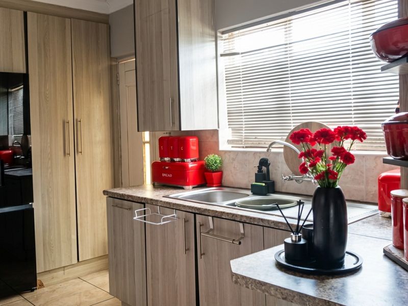 A modern kitchen featuring light wood-grain cabinetry, laminate countertops, a stainless steel sink, and tiled flooring with ample storage space.