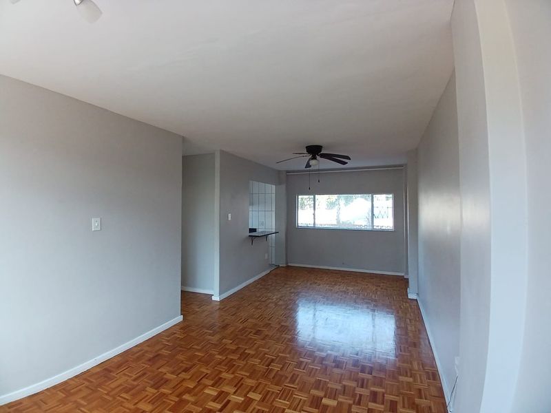 Spacious open-plan living area featuring classic parquet flooring, a ceiling fan, and a convenient breakfast bar connecting to the kitchen space.