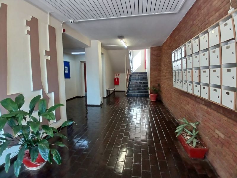 A communal apartment building entrance lobby featuring a brick wall, a bank of mailboxes, tiled flooring, and a staircase leading to upper levels.