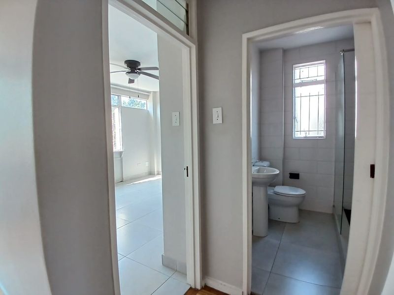 A bright hallway providing access to a bedroom and a bathroom featuring a pedestal basin, toilet, and shower enclosure.