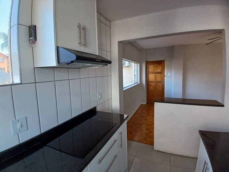 A clean, functional kitchen featuring white cabinetry, dark granite countertops, an integrated hob, and an extractor fan, leading into an adjacent living area.