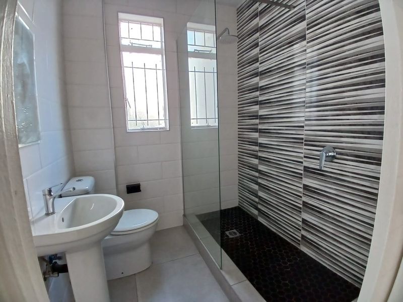 Modern bathroom featuring a walk-in shower with a rain shower head, mosaic floor tiles, pedestal basin, and toilet.