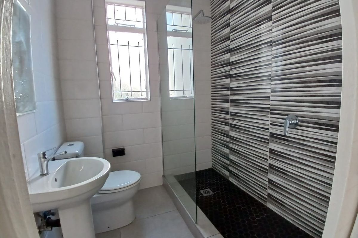 Modern bathroom featuring a walk-in shower with a rain shower head, mosaic floor tiles, pedestal basin, and toilet.