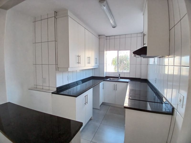 A clean, modern kitchen featuring white cabinetry, dark granite countertops, tiled walls, and an integrated extractor fan in a bright, functional layout.