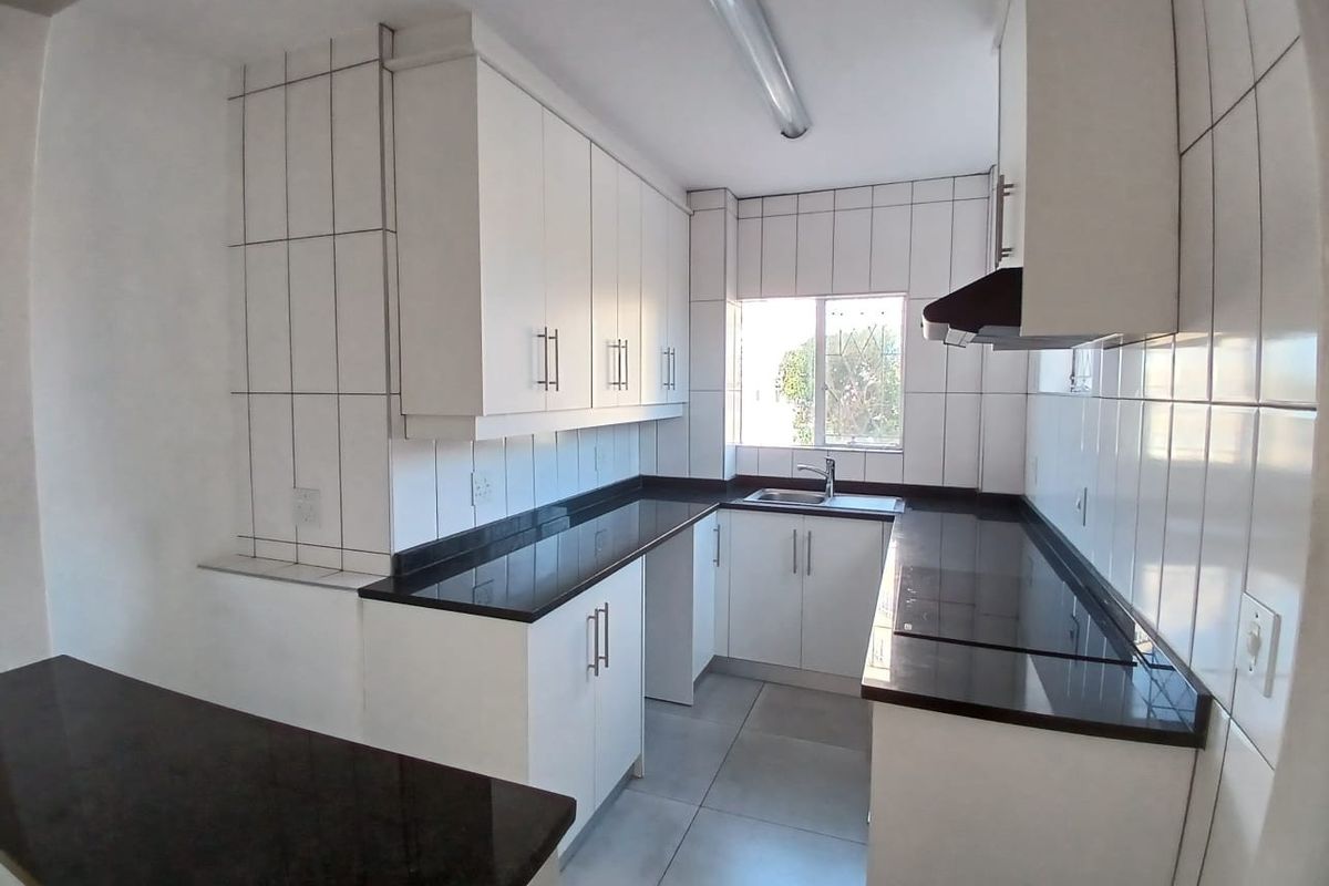 A clean, modern kitchen featuring white cabinetry, dark granite countertops, tiled walls, and an integrated extractor fan in a bright, functional layout.