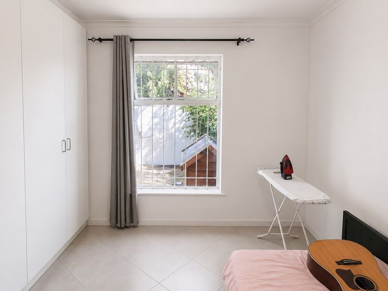 A clean bedroom featuring built-in cupboards, tiled flooring, and a window fitted with security bars.