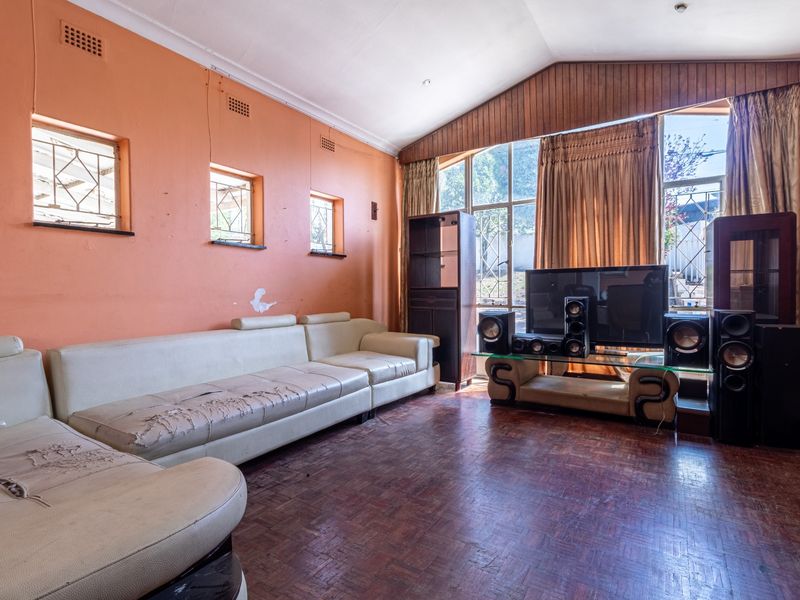 A spacious living room featuring parquet flooring, a vaulted ceiling, and large windows that provide ample natural light.